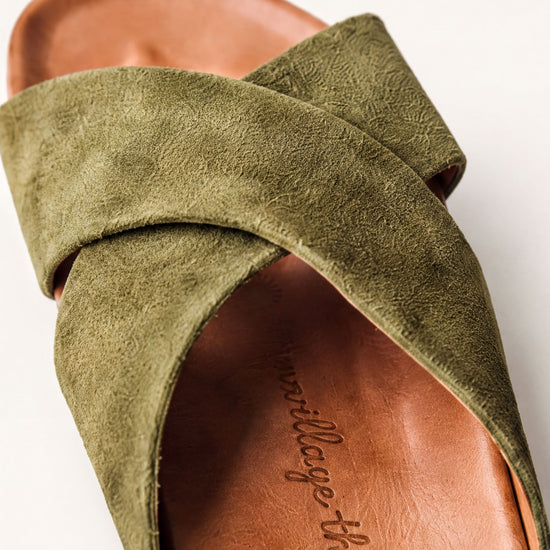 A close-up view of a green suede sandal with a textured pattern on the strap.
