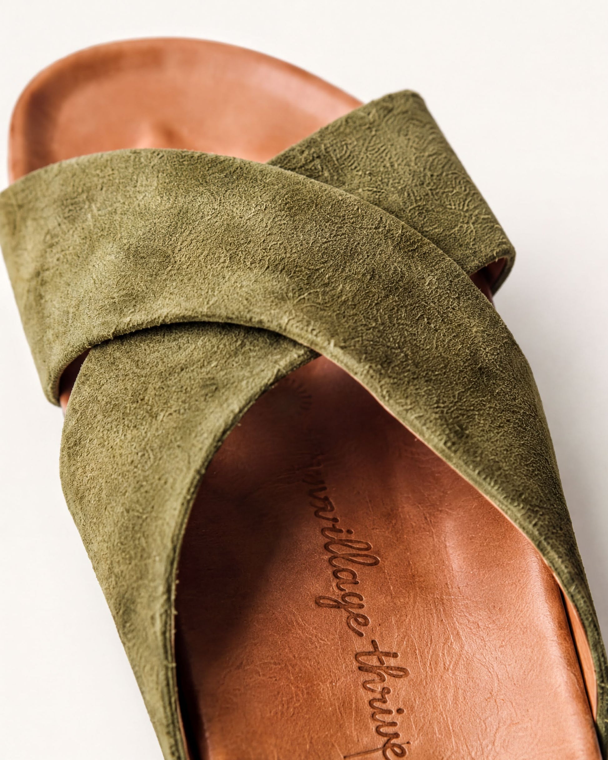 A close-up view of a green suede sandal with a textured pattern on the strap.