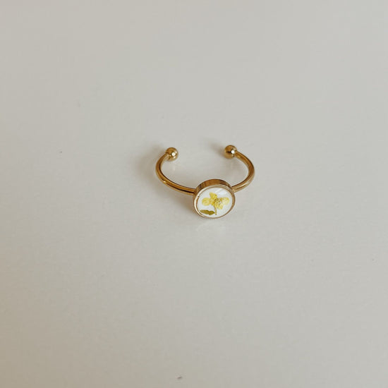 Gold ring with a round white stone on a light gray background
