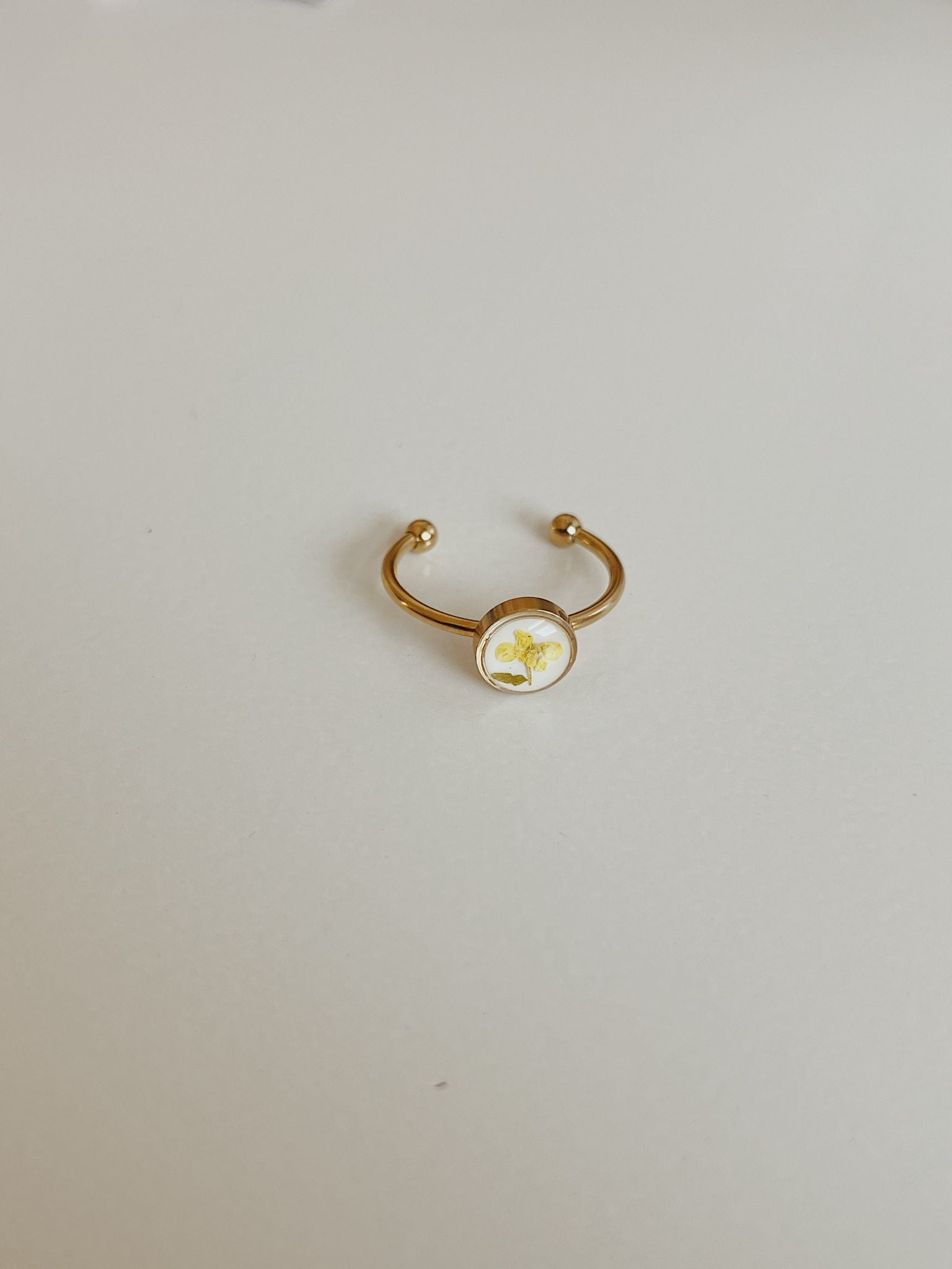 Gold ring with a round white stone on a light gray background