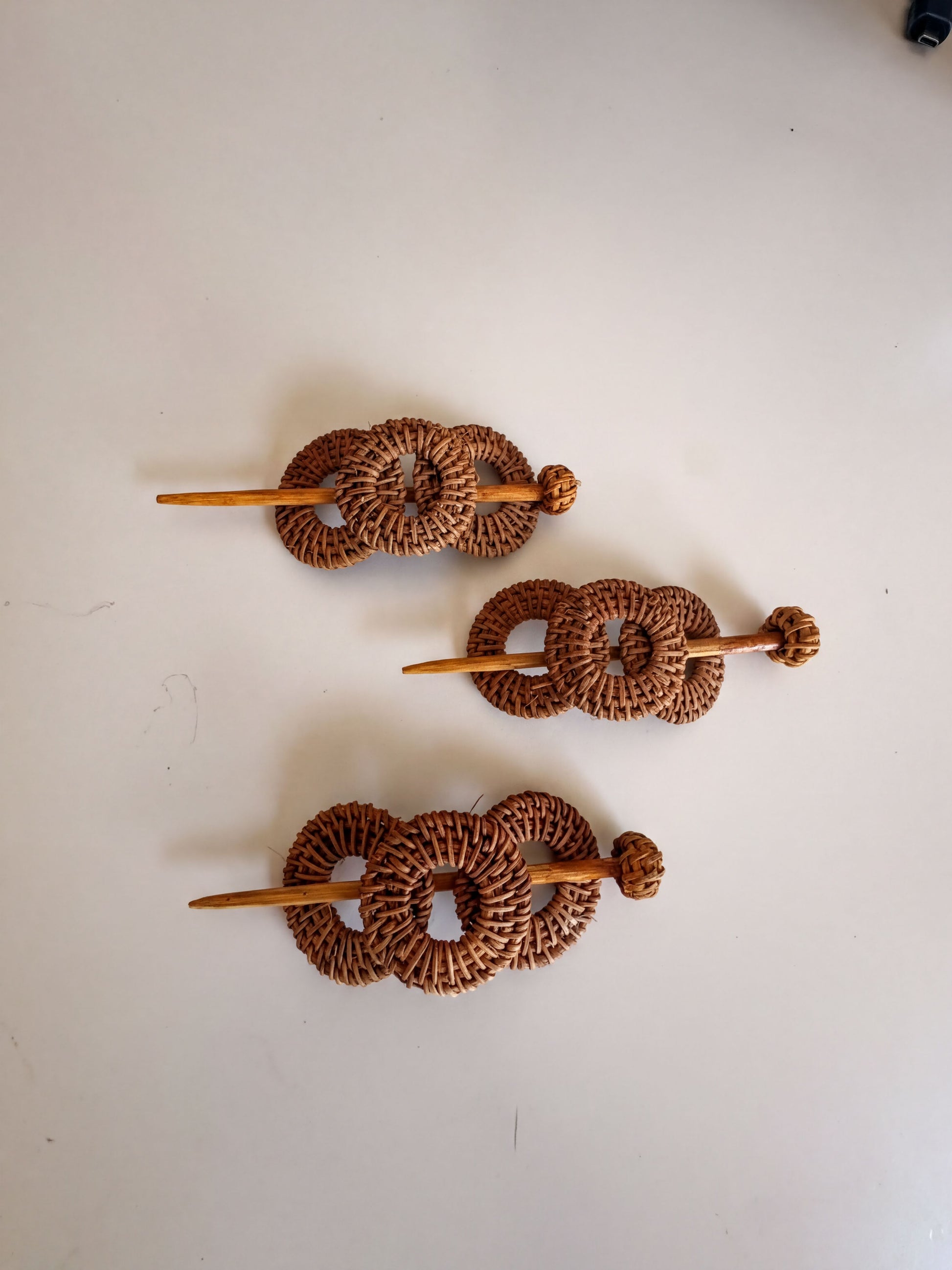 Three woven hair clips made of brown wicker material, each with a wooden stick.