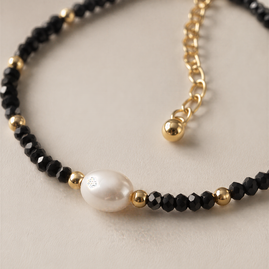 A delicate bracelet with black beads and a single white pearl bead.
