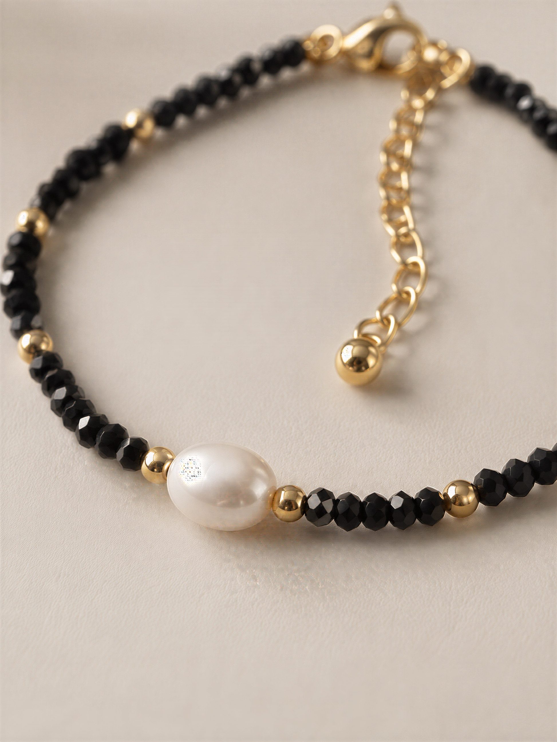 A delicate bracelet with black beads and a single white pearl bead.