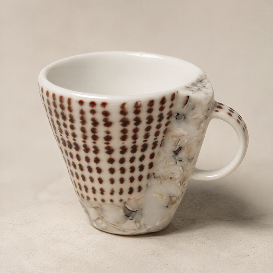 A white ceramic mug with a unique brown and white polka dot pattern on its side, sitting on a plain surface.