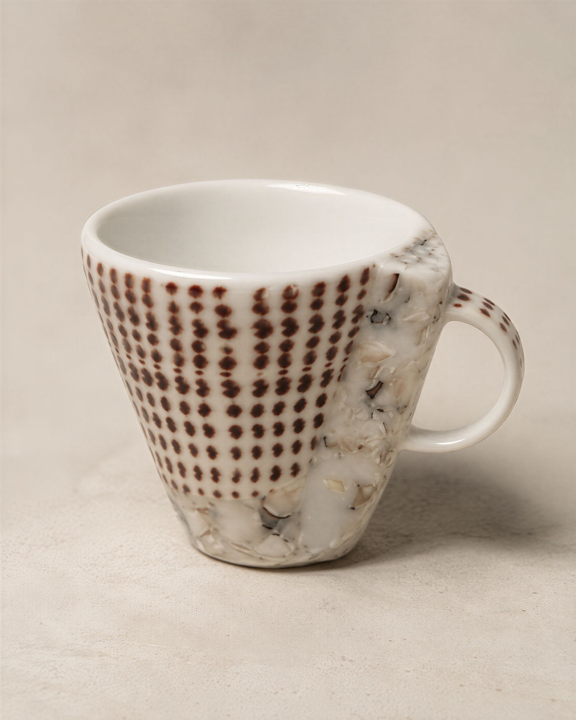 A white ceramic mug with a unique brown and white polka dot pattern on its side, sitting on a plain surface.