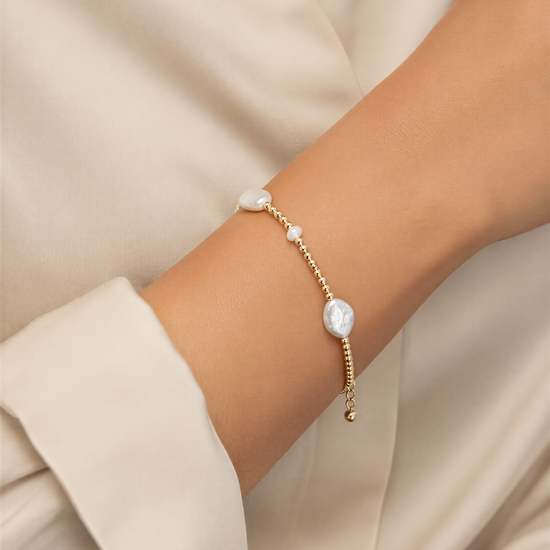 A close-up view of a person's arm wearing a delicate gold-toned bracelet with small white pearls.