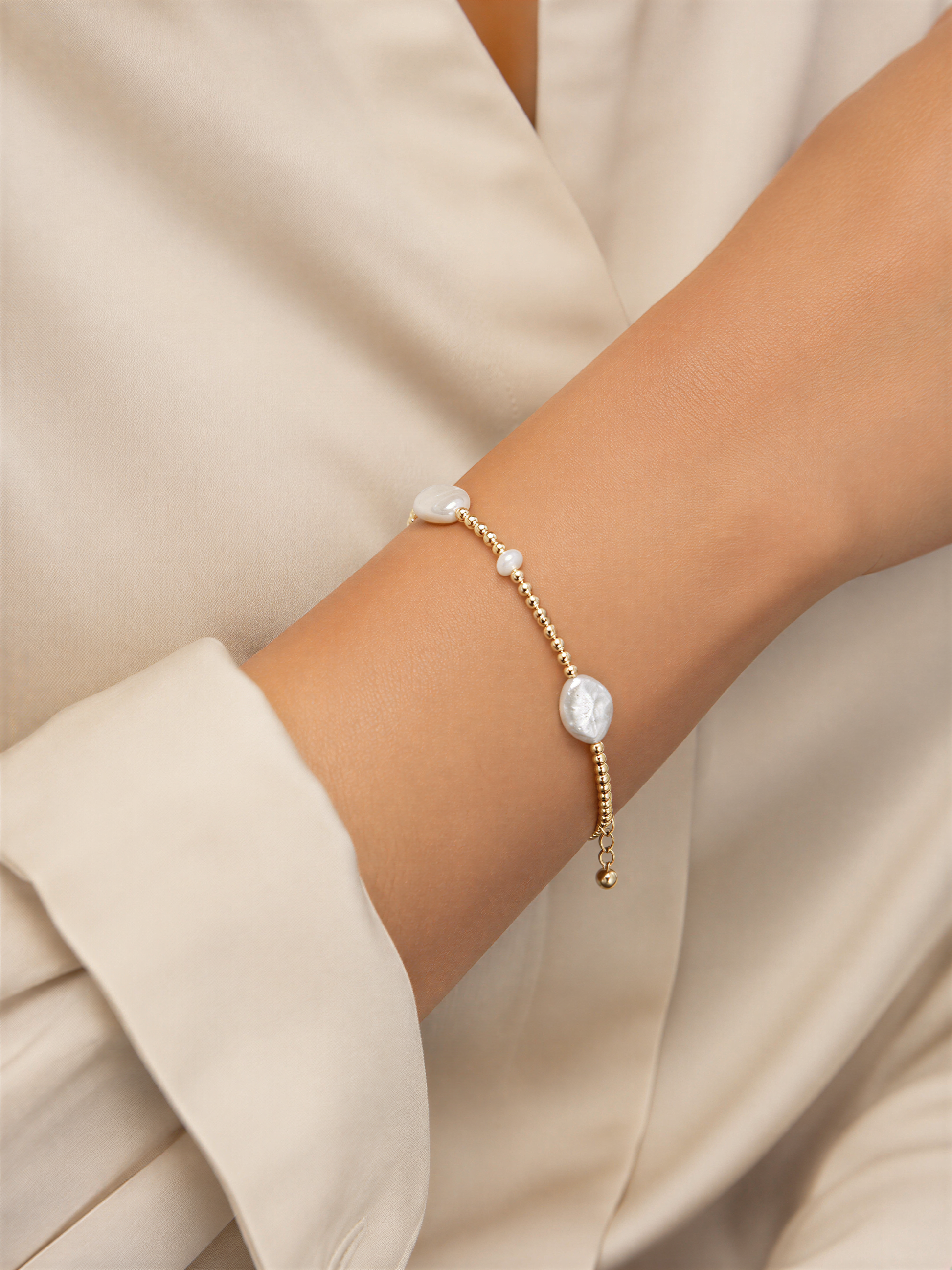A close-up view of a person's arm wearing a delicate gold-toned bracelet with small white pearls.