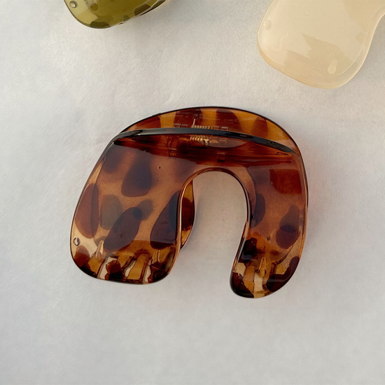 A brown, spotted object resembling a piece of jewelry or a decorative item is shown on a white surface.