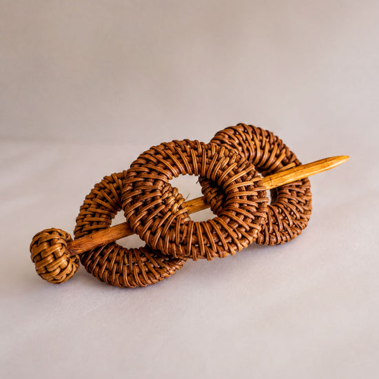 A woven hair accessory consisting of three circular pieces connected by a wooden stick.
