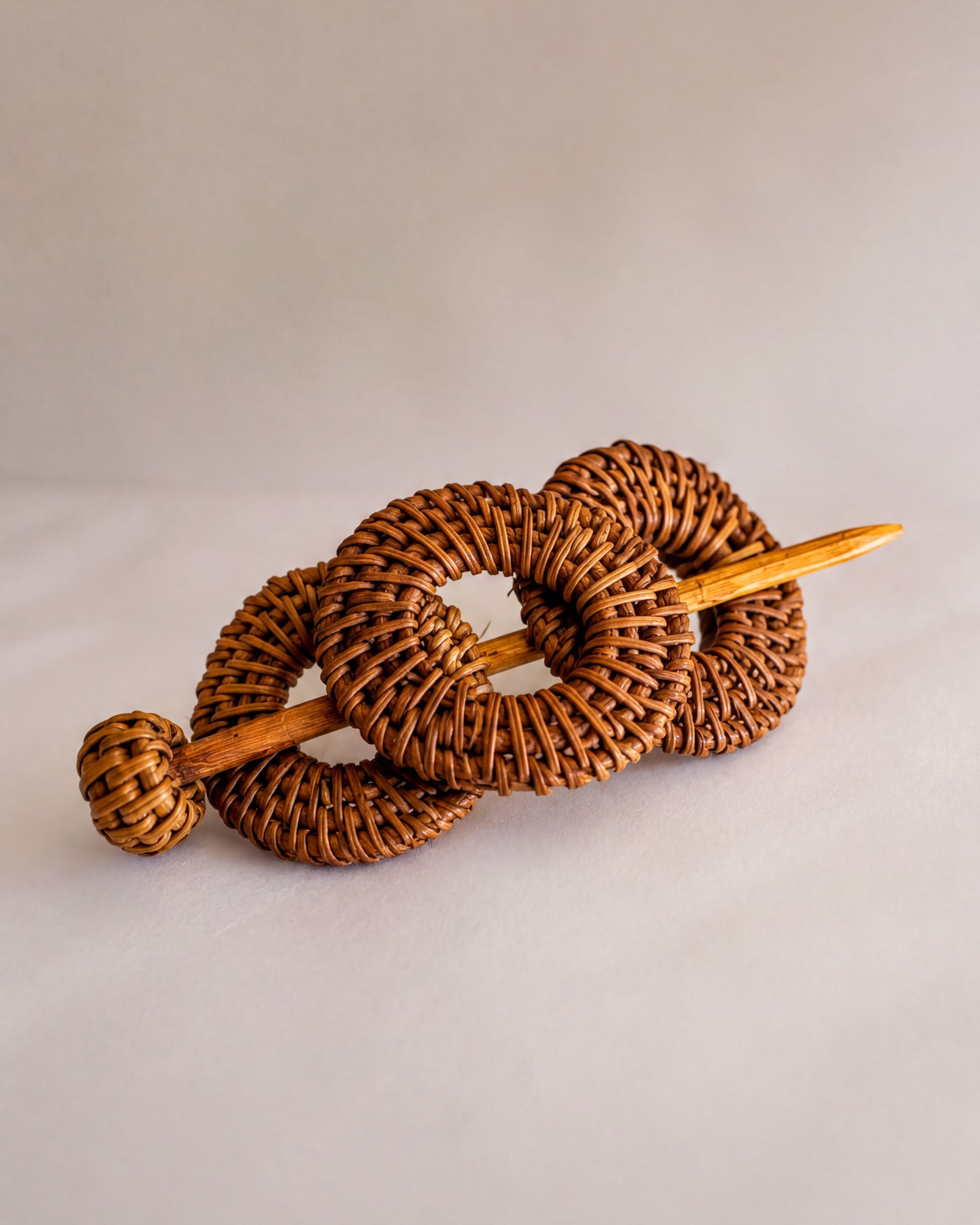 A woven hair accessory consisting of three circular pieces connected by a wooden stick.