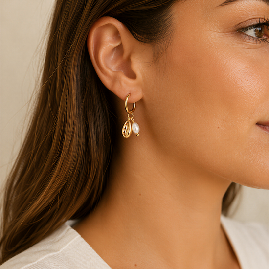 A close-up of a woman's face wearing a pair of gold earrings with pearls and charms hanging from them.