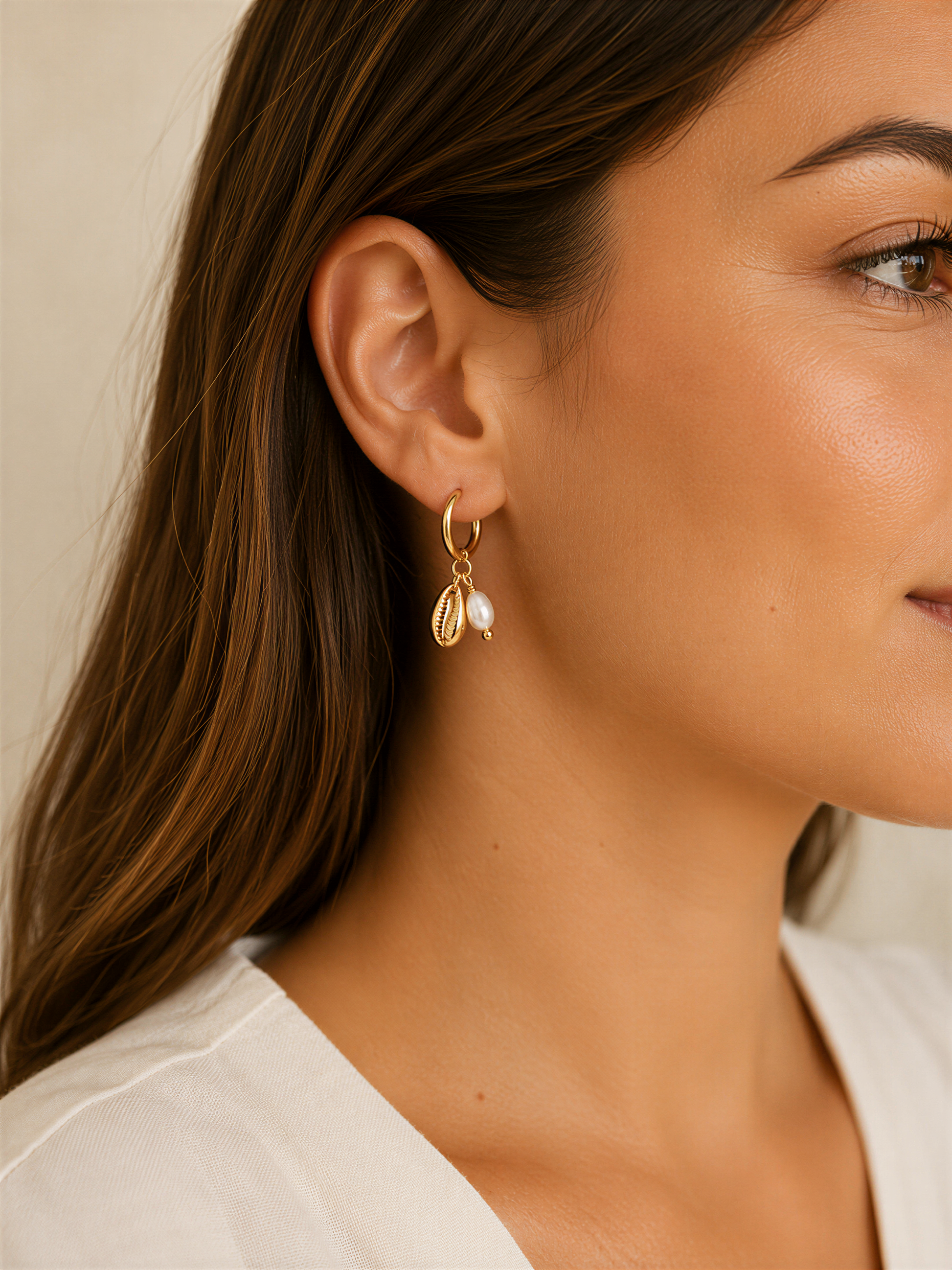 A close-up of a woman's face wearing a pair of gold earrings with pearls and charms hanging from them.