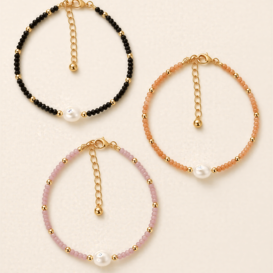 Three beaded bracelets with pearls and gold-colored charms, each with a unique color and design.