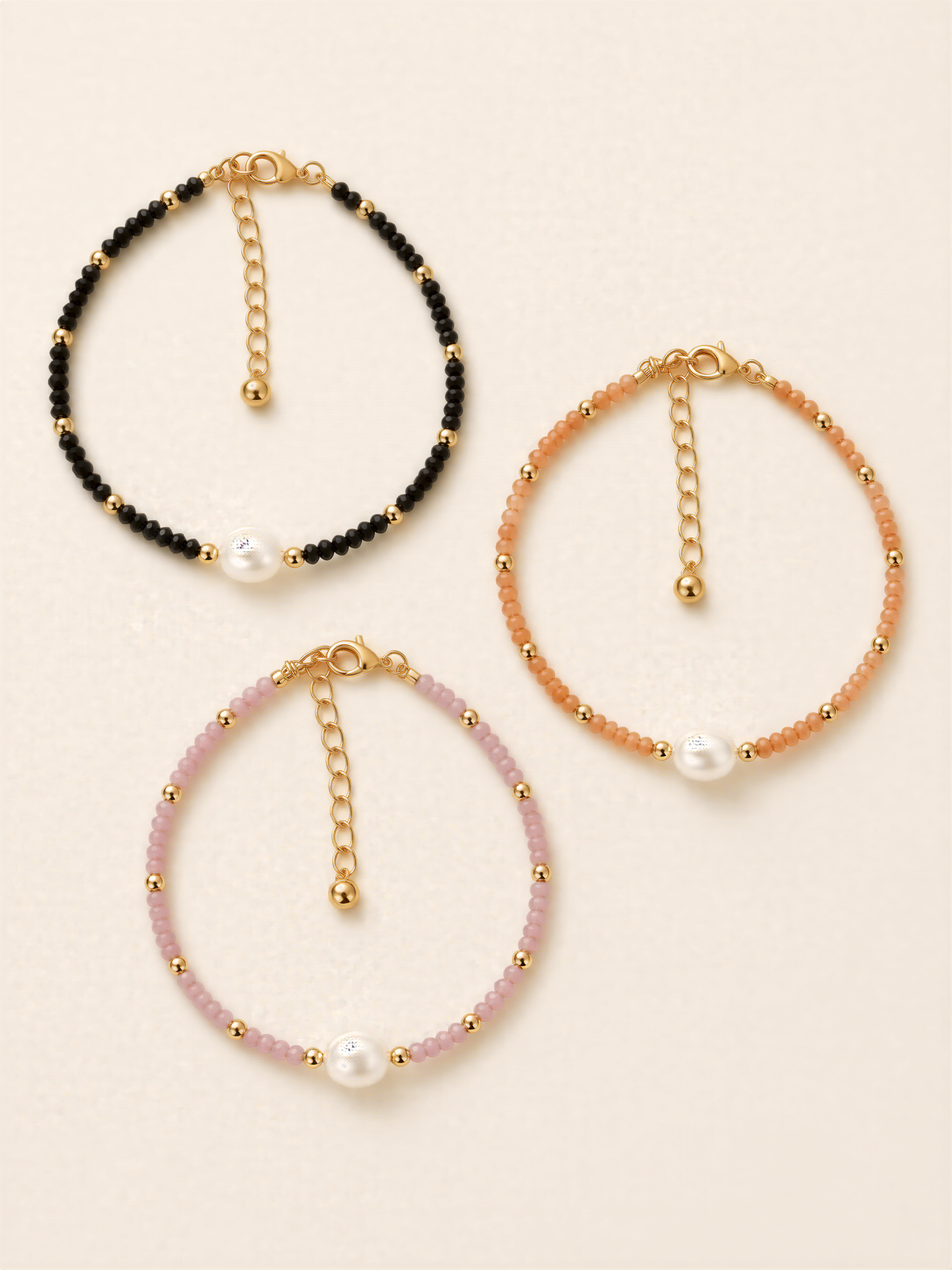 Three beaded bracelets with pearls and gold-colored charms, each with a unique color and design.