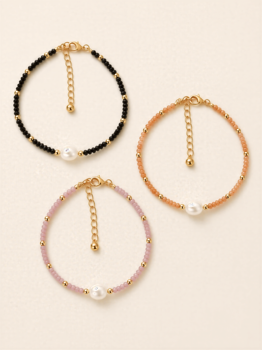Three beaded bracelets with pearls and gold-colored charms, each with a unique color and design.
