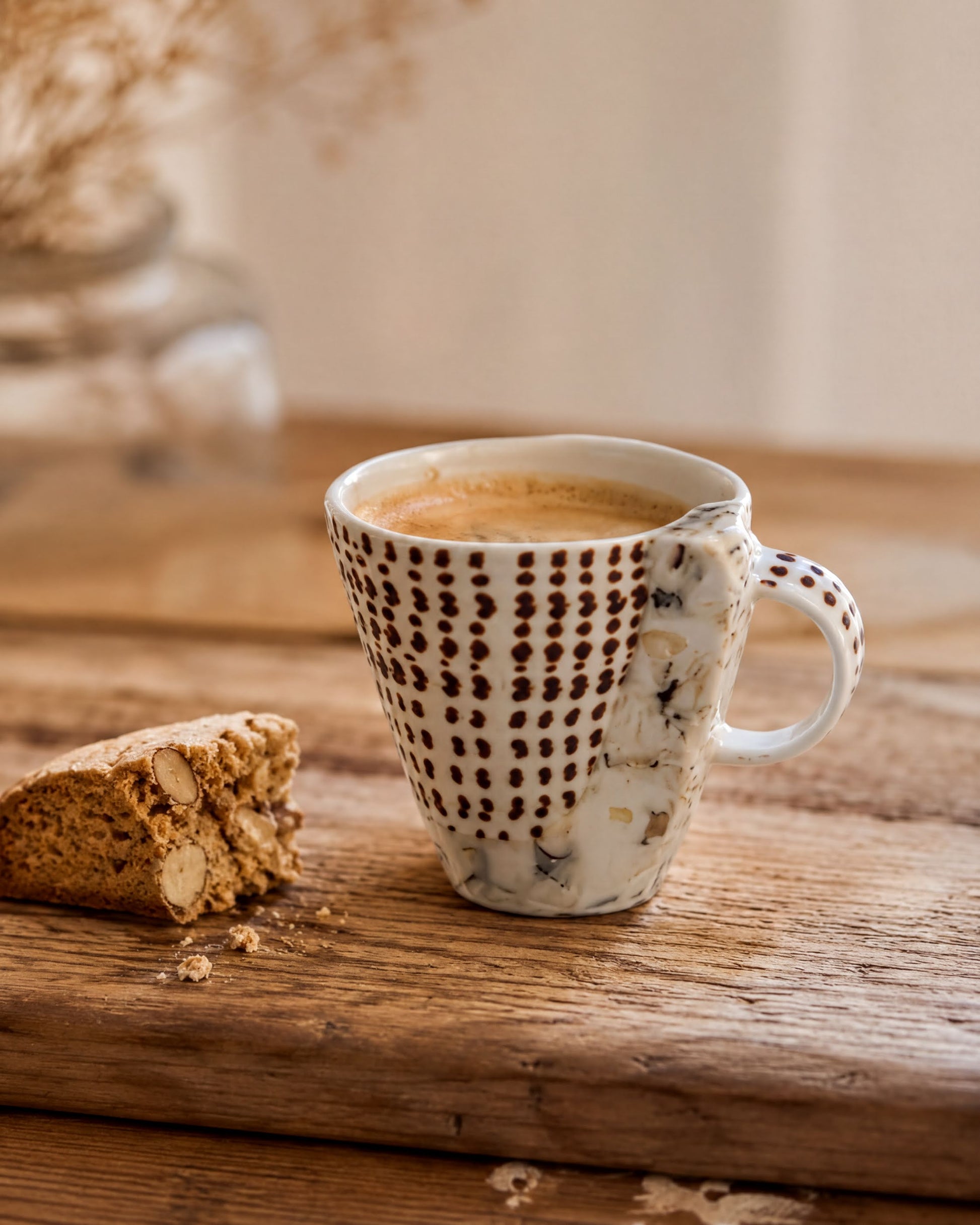 A white mug with a black and white polka dot pattern sits on a wooden surface, with a partially eaten cookie beside it.