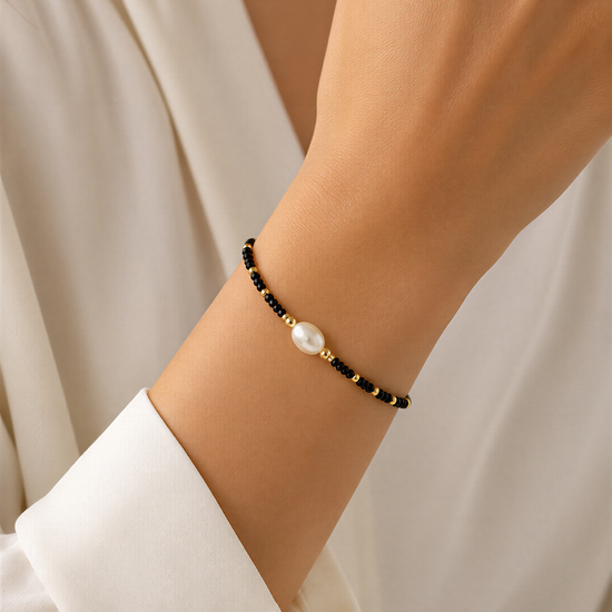A close-up view of a person's wrist wearing a black and gold bead bracelet with a single pearl bead.