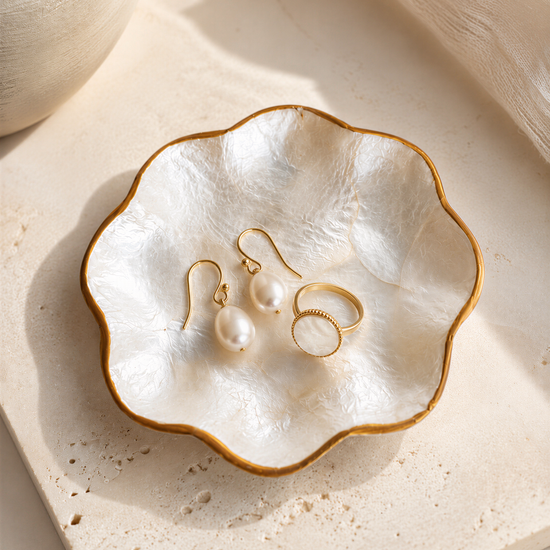 A white bowl with a gold rim containing a pair of pearl earrings and a ring.
