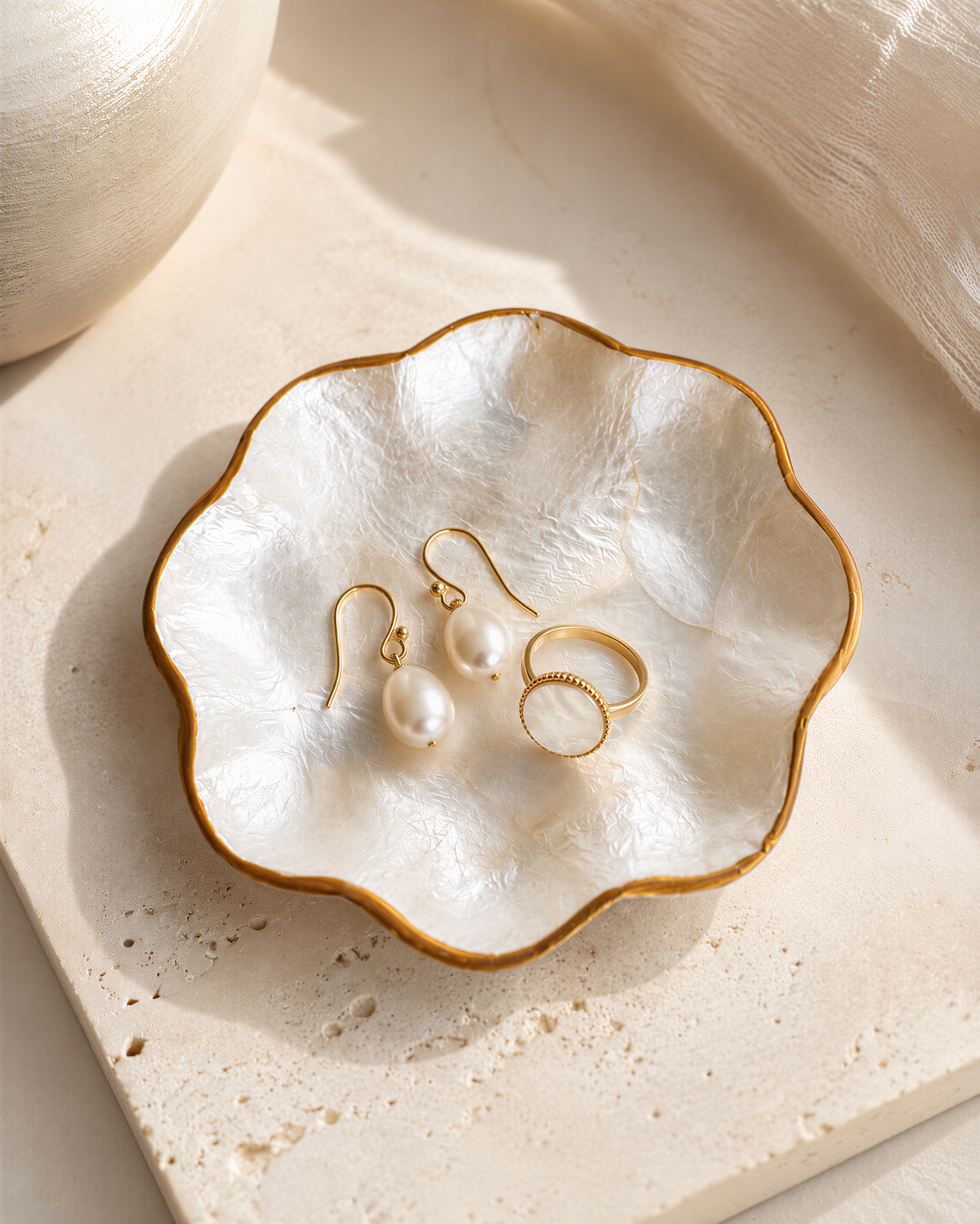 A white bowl with a gold rim containing a pair of pearl earrings and a ring.