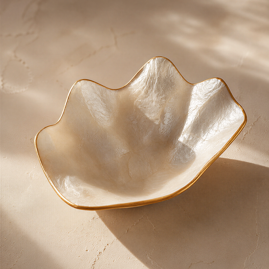 A white, oval-shaped bowl with a gold rim sits on a textured surface, casting a shadow.