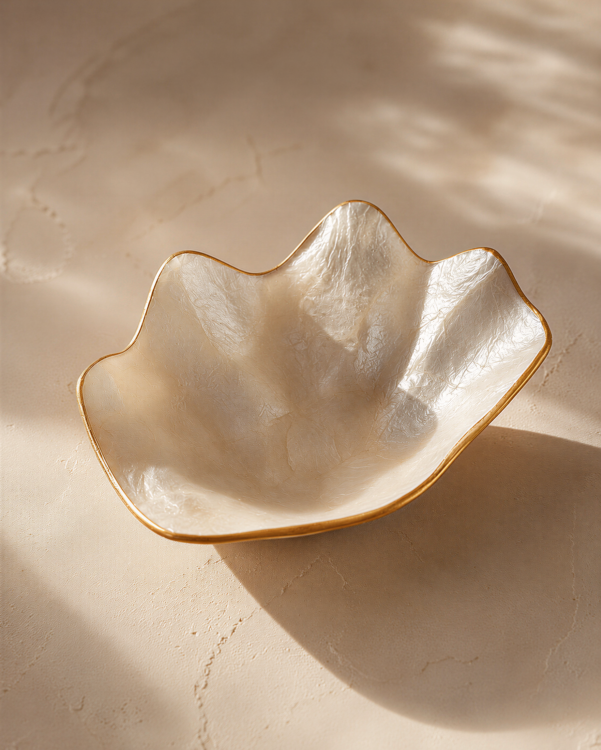 A white, oval-shaped bowl with a gold rim sits on a textured surface, casting a shadow.