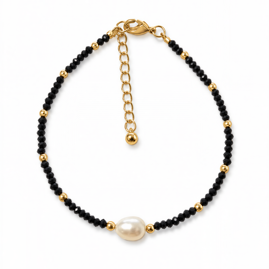 A gold-colored bracelet with black beads and a single white pearl bead.