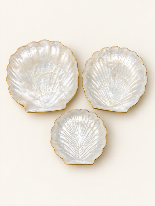 Three white seashell-shaped plates with gold trim are arranged in a triangular formation on a light background.