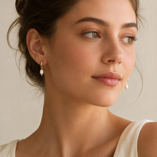 A close-up portrait of a woman with dark hair, wearing a white top and earrings with a pearl design.