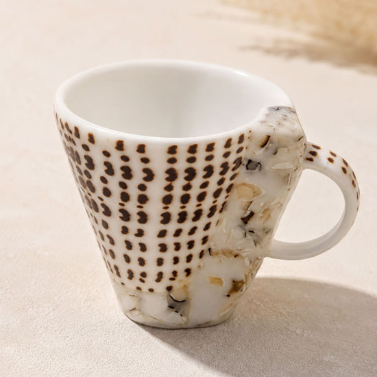 A white ceramic mug with a pattern of brown dots on a beige background.