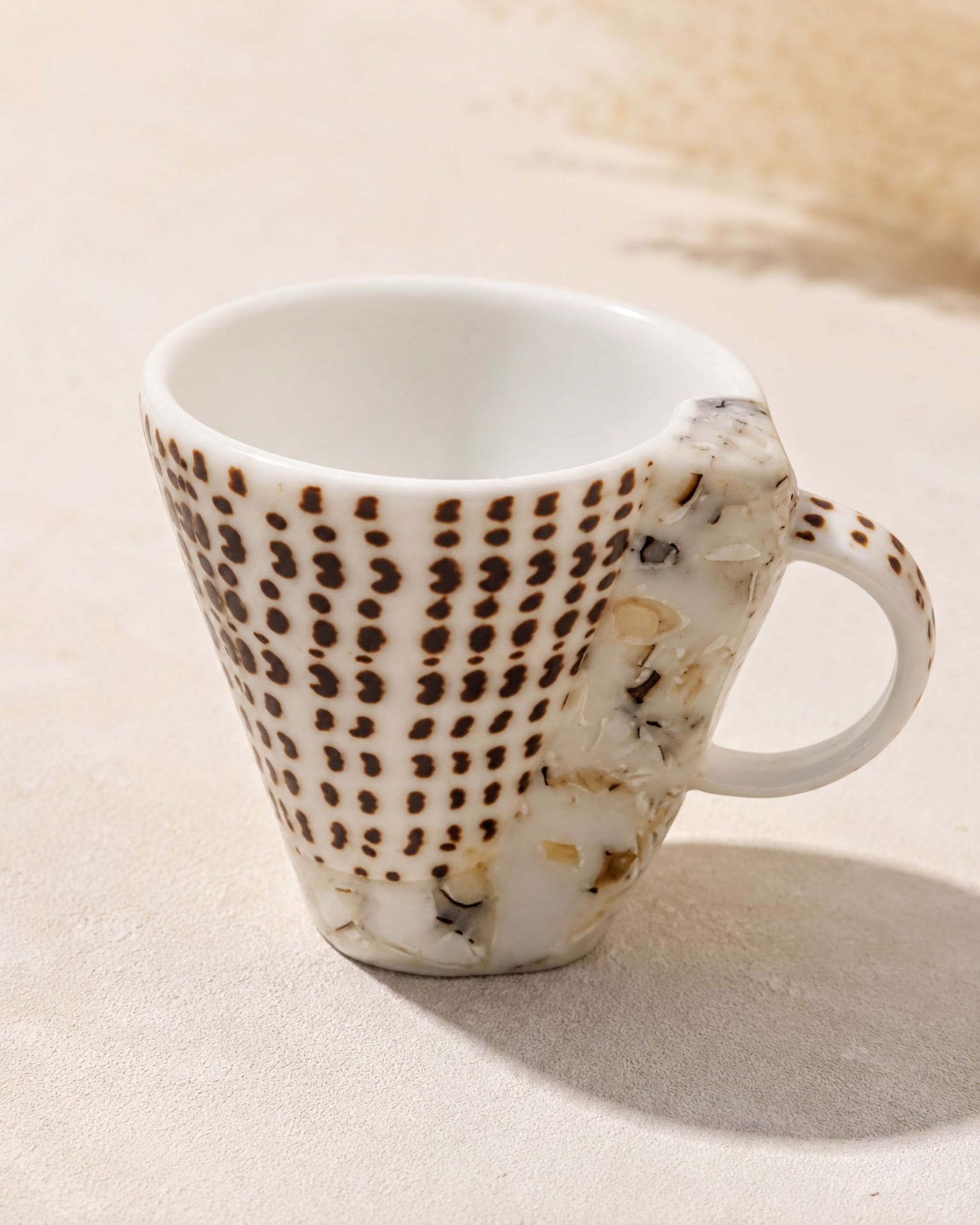 A white ceramic mug with a pattern of brown dots on a beige background.